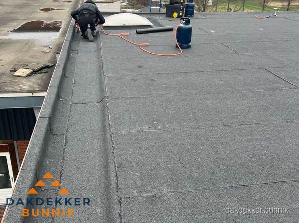 Dakdekker repareert bitumen dakbedekking op groot plat dak in Bunnik