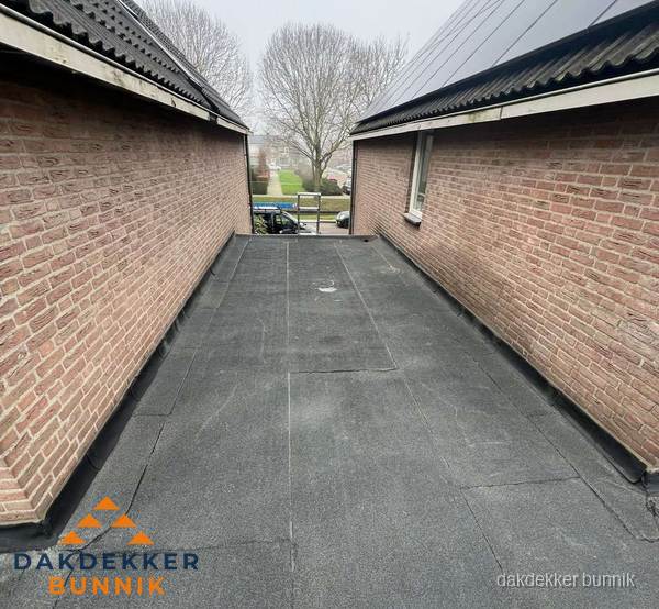 Plat dak met bitumen dakbedekking tussen bakstenen muren in Bunnik
